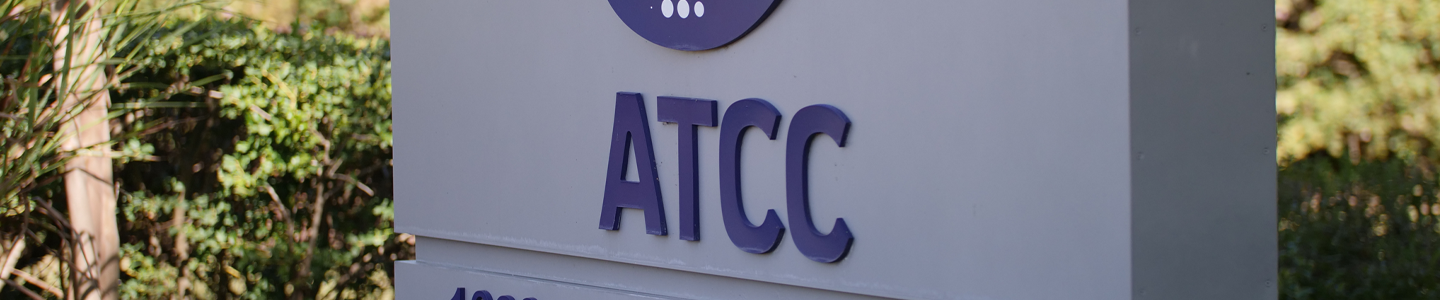 Exterior vertical gray cement rectangle sign with ATCC logo and "ATCC, 10801 University Boulevard" near green shrubbery.
