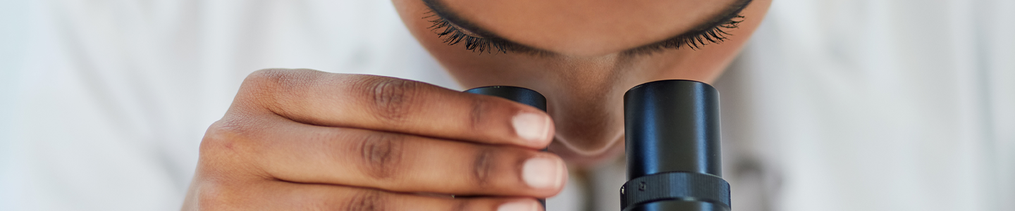 Scientist looking into a microscope, hand on one of the eye pieces.