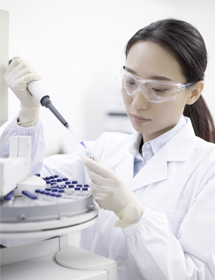 Scientist wearing lab coat, safety glasses, and gloves, holding pipette and vial next to centrifuge.