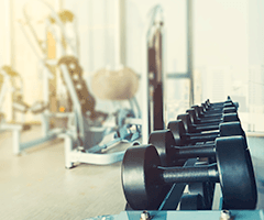 A row of black dumb bells on a stand with gym fitness equipment in the background.