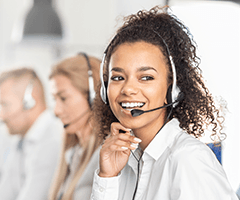 Young, black woman wearing a head set smiling with other people wearing head sets in the background.