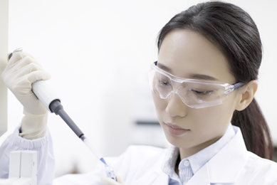 Scientist wearing lab coat, safety glasses, and gloves, holding pipette and vial next to centrifuge.