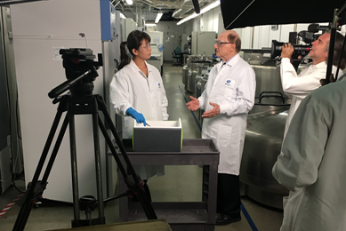 ATCC scientist with gloved hand in cooler on cart talking with Dr. Cypess, camera crew around them during filming in biorepository.
