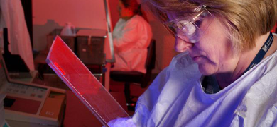 Side view of scientist in gown and gloves holding a pipette controller over tubes in a tray.