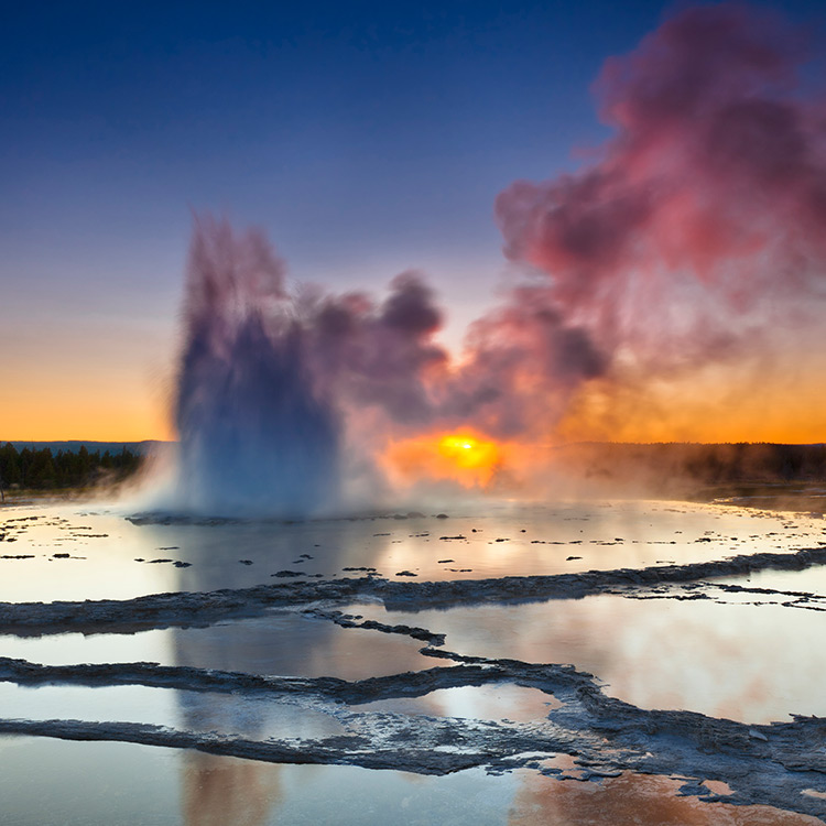 Great-Fountain-Geysir A plume of smoke rising from layers of slate-like liquid at Great Fountain Geyser in Yellowstone National Park at sunset.
