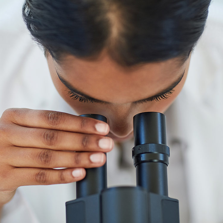 Scientist looking into a microscope, hand on one of the eye pieces.